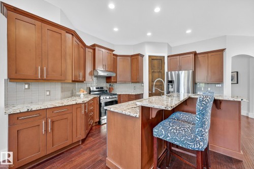Kitchen featuring brown cabinets, a breakfast bar, appliances with stainless steel finishes, dark wood-type flooring, and light stone countertops - 940 Haliburton Road, Edmonton, AB - Indoor Photo Showing Kitchen With Double Sink With Upgraded Kitchen