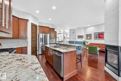 Kitchen featuring light stone countertops, a kitchen island with sink, a multi sided fireplace, brown cabinets, and recessed lighting - 940 Haliburton Road, Edmonton, AB - Indoor Photo Showing Kitchen With Fireplace