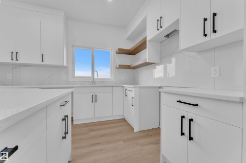 White cabinetry with matte black hardware, light wood-finish flooring, white countertop surfaces, and a tiled backsplash - 285 Munn Way, Leduc, AB - Indoor Photo Showing Kitchen