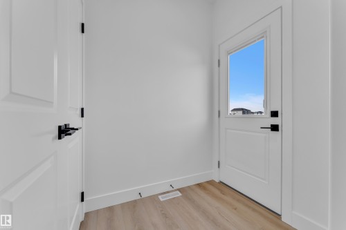 Entryway featuring a white door with an upper glass panel, a second white paneled door, black hardware throughout, wood-finish flooring, and white baseboards - 285 Munn Way, Leduc, AB - Indoor Photo Showing Other Room