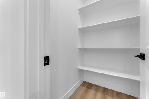 Pantry with multiple white shelves, light wood-finish flooring, white baseboards, and matte black door hardware - 285 Munn Way, Leduc, AB - Indoor With Storage