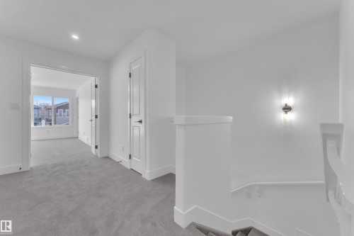 Carpeted hallway with white walls and trim, featuring a recessed light and a wall sconce - 285 Munn Way, Leduc, AB - Indoor Photo Showing Other Room