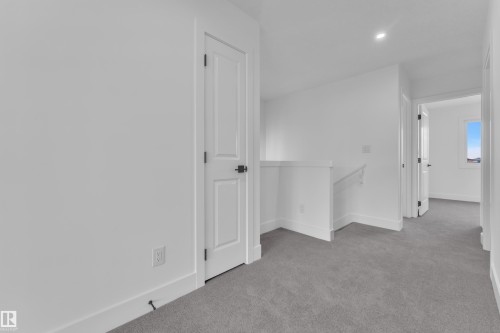 Carpeted hallway featuring white walls, white doors with dark hardware, a white railing, and recessed ceiling lighting - 285 Munn Way, Leduc, AB - Indoor Photo Showing Other Room