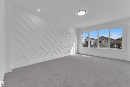 Spacious room featuring a decorative accent wall with a geometric pattern, large multi-pane windows, recessed lighting, a modern flush-mount ceiling light, and light gray carpeting - 285 Munn Way, Leduc, AB - Indoor