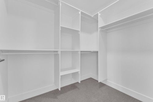 Walk-in closet featuring white built-in shelving, multiple hanging rods, and gray carpet flooring - 285 Munn Way, Leduc, AB - Indoor With Storage