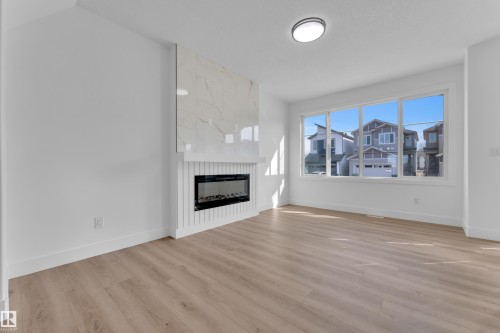 Living area featuring wood-finish flooring, a contemporary electric fireplace with a white shiplap-style surround and a large-format tile accent, a prominent window assembly, and a flush-mount ceiling light - 285 Munn Way, Leduc, AB - Indoor Photo Showing Living Room With Fireplace
