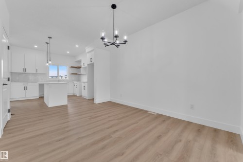 Open-concept living space featuring wood-finish flooring, a contemporary black chandelier, a kitchen island, white cabinetry, and a white subway tile backsplash - 285 Munn Way, Leduc, AB - Indoor Photo Showing Kitchen With Upgraded Kitchen