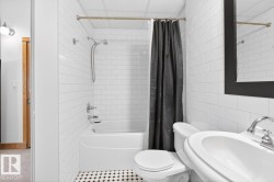 Bathroom featuring a white subway tile surround, a built-in bathtub with shower, a vanity sink with chrome fixtures, and black and white checkerboard floor tiling - 