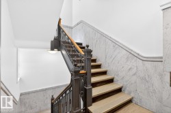 Grand staircase featuring stone treads, an ornate dark wood and metal balustrade, and a natural wood handrail - 