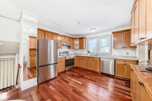 The kitchen features hardwood floors, light-colored wooden cabinetry, and stainless steel appliances including a refrigerator, stove, and dishwasher - 8733 181A Street Nw, Edmonton, AB - Indoor Photo Showing Kitchen