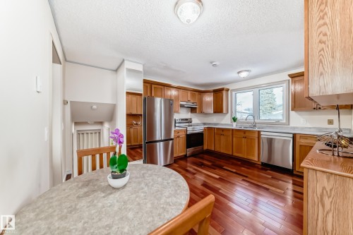 The kitchen features wood cabinetry, stainless steel appliances, and rich wood flooring - 8733 181A Street Nw, Edmonton, AB - Indoor