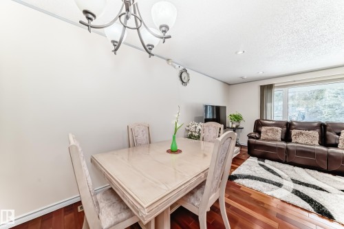 This dining area features hardwood floors and a chandelier, with a living area visible in the background - 8733 181A Street Nw, Edmonton, AB - Indoor Photo Showing Dining Room