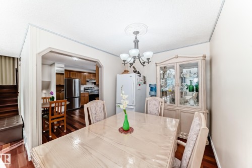 The dining area features hard flooring and an ornamental chandelier, with a view into the kitchen, which includes stainless steel appliances - 8733 181A Street Nw, Edmonton, AB - Indoor Photo Showing Dining Room