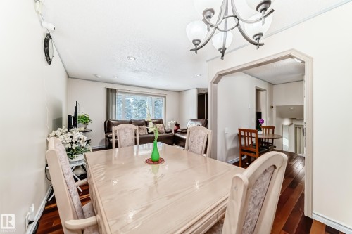 The property features an inviting dining area with a chandelier and rich hardwood flooring, offering a clear view into a living area with a large window - 8733 181A Street Nw, Edmonton, AB - Indoor Photo Showing Dining Room