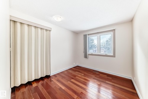 This room features rich hardwood flooring, a window providing views of trees and houses, and a ceiling light fixture - 8733 181A Street Nw, Edmonton, AB - Indoor Photo Showing Other Room
