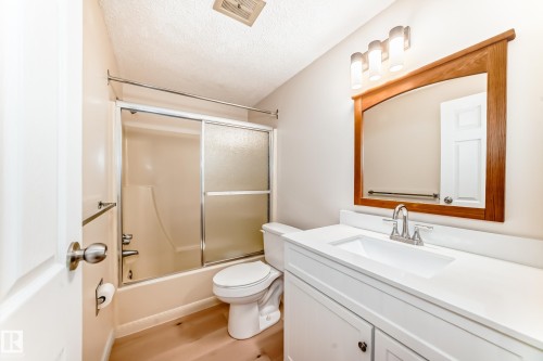 The bathroom features a vanity with a white countertop and a mirror with a wooden frame - 8733 181A Street Nw, Edmonton, AB - Indoor Photo Showing Bathroom