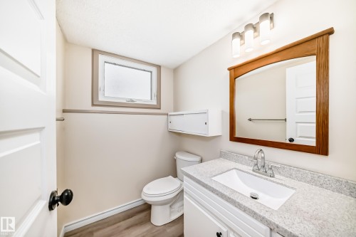 Bathroom featuring a white vanity with a light-colored countertop, a toilet, a window with a light-colored trim, and a mirror with a wooden frame - 8733 181A Street Nw, Edmonton, AB - Indoor Photo Showing Bathroom