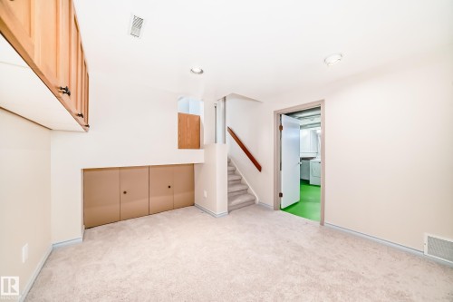 This room features neutral-toned carpeting, a light wood handrail along the carpeted stairs, and built-in cabinetry - 8733 181A Street Nw, Edmonton, AB - Indoor Photo Showing Other Room