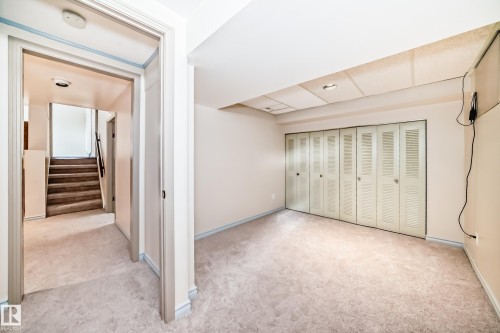 This room features neutral-toned carpeting, a wall of louvered bifold closet doors, and a drop ceiling - 8733 181A Street Nw, Edmonton, AB - Indoor Photo Showing Other Room