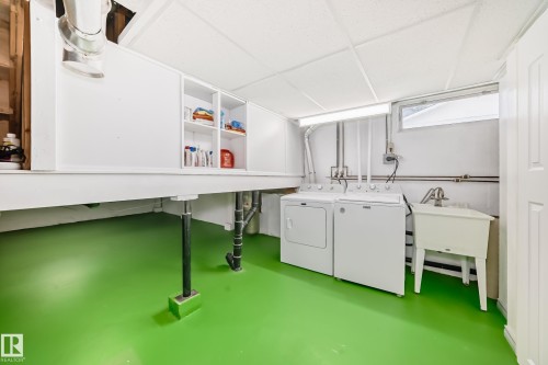 This utility room features a washer and dryer, a laundry sink, and built-in storage shelving - 8733 181A Street Nw, Edmonton, AB - Indoor Photo Showing Laundry Room