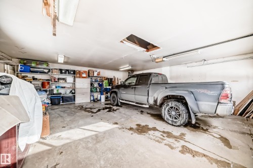 This property features a spacious garage with exposed ceiling joists and fluorescent lighting - 8733 181A Street Nw, Edmonton, AB - Indoor Photo Showing Garage