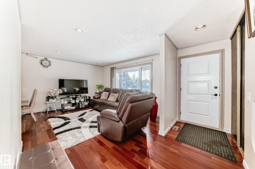 The property features rich hardwood flooring, a white paneled front door, and a spacious living area with a large window - 8733 181A Street Nw, Edmonton, AB - Indoor Photo Showing Other Room