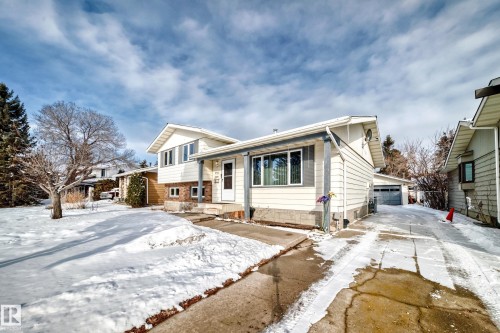 This property features a light-colored exterior with brick accents, large windows, and a driveway leading to a garage - 8733 181A Street Nw, Edmonton, AB - Outdoor