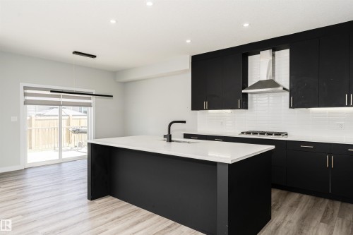 Contemporary kitchen featuring black cabinetry, white countertops, a white subway tile backsplash, and a central island with an undermount sink - 5386 Kimball Place, Edmonton, AB - Indoor Photo Showing Kitchen With Upgraded Kitchen