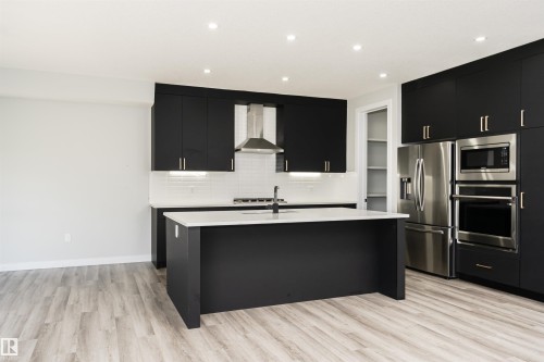 Contemporary kitchen featuring matte black cabinetry with brushed gold hardware, stainless steel appliances, a center island with a white countertop, and light wood-finish flooring - 5386 Kimball Place, Edmonton, AB - Indoor Photo Showing Kitchen With Upgraded Kitchen