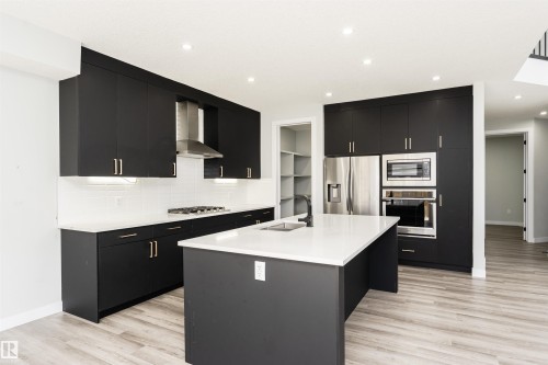 Modern kitchen featuring dark cabinetry, stainless steel appliances, a center island with sink, white countertops, and wood-finish flooring - 5386 Kimball Place, Edmonton, AB - Indoor Photo Showing Kitchen With Double Sink With Upgraded Kitchen