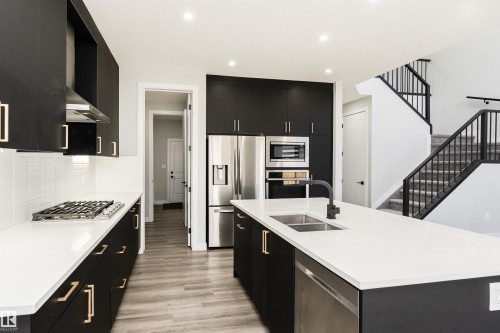 Modern kitchen featuring black cabinetry with gold-tone hardware, white countertops, and stainless steel appliances - 5386 Kimball Place, Edmonton, AB - Indoor Photo Showing Kitchen With Double Sink With Upgraded Kitchen