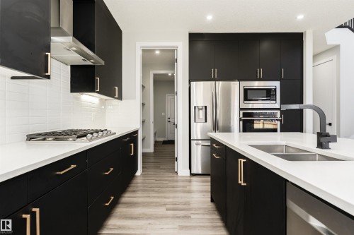 Modern kitchen featuring dark cabinetry with gold-toned hardware, white countertops, and light wood-finish flooring - 5386 Kimball Place, Edmonton, AB - Indoor Photo Showing Kitchen With Double Sink With Upgraded Kitchen
