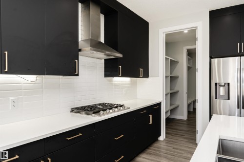 Modern kitchen featuring black cabinetry with gold-toned hardware, white solid surface countertops, and white subway tile backsplash - 5386 Kimball Place, Edmonton, AB - Indoor Photo Showing Kitchen With Upgraded Kitchen