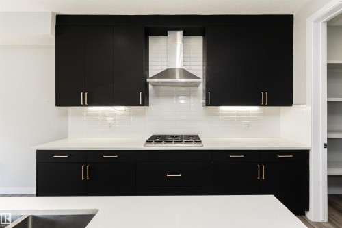 Contemporary kitchen showcasing matte black cabinetry with gold-tone hardware, white countertops, a subway tile backsplash, a gas cooktop, and a stainless steel range hood - 5386 Kimball Place, Edmonton, AB - Indoor Photo Showing Kitchen With Double Sink