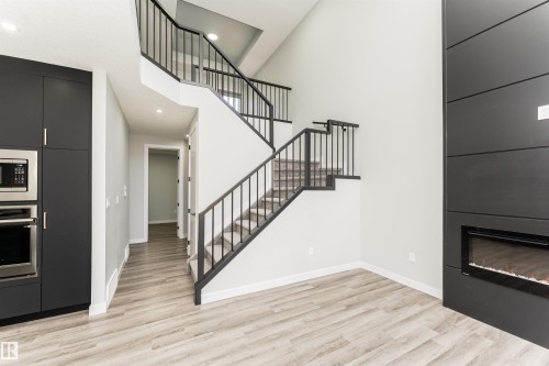 Two-story open concept space featuring a contemporary staircase with black metal railings, light wood-finish flooring, a built-in wall oven and microwave combination, a built-in electric fireplace, and recessed lighting - 5386 Kimball Place, Edmonton, AB - Indoor With Fireplace