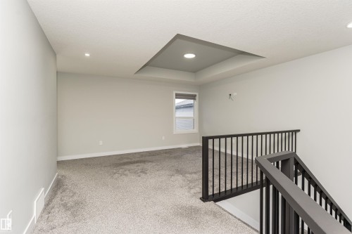 Recessed tray ceiling with integrated lighting, window with horizontal blinds, gray carpeted flooring, and dark-toned open railing - 5386 Kimball Place, Edmonton, AB - Indoor Photo Showing Other Room
