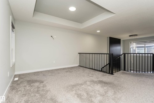 Carpeted upper level featuring a tray ceiling with recessed lighting, black metal railings, and a large window - 5386 Kimball Place, Edmonton, AB - Indoor Photo Showing Other Room