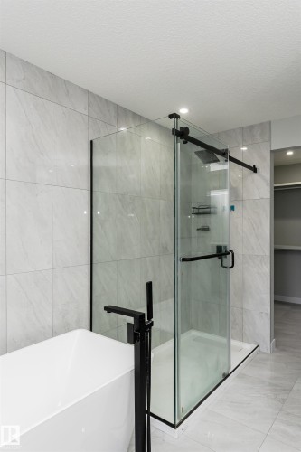 Contemporary bathroom featuring a freestanding tub with a matte black floor-mounted filler, a glass-enclosed shower with a matte black rain shower head, and large format wall and floor tile - 5386 Kimball Place, Edmonton, AB - Indoor Photo Showing Bathroom