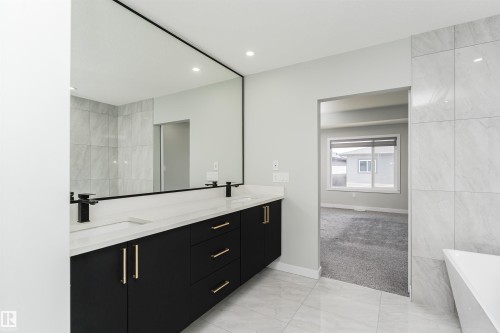 Dual vanity featuring dark cabinetry with gold-tone hardware, white countertops, and matte black fixtures - 5386 Kimball Place, Edmonton, AB - Indoor Photo Showing Bathroom