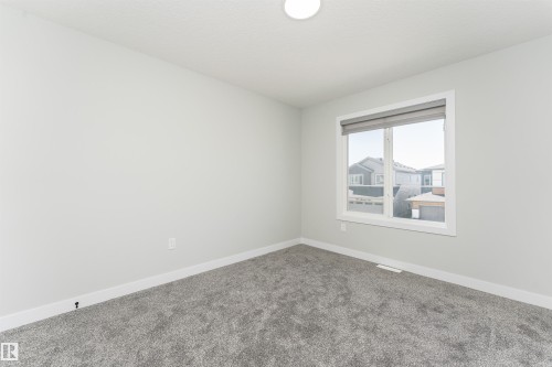 Carpeted room featuring a white-framed window with a grey roller blind, light grey painted walls, and white baseboards - 5386 Kimball Place, Edmonton, AB - Indoor Photo Showing Other Room