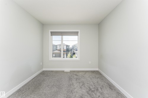 Neutral-toned room featuring a large window with a roller shade, light gray carpeting, crisp white baseboards, and a single wall outlet - 5386 Kimball Place, Edmonton, AB - Indoor Photo Showing Other Room