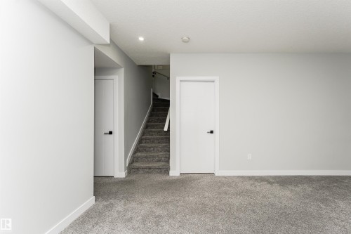 Carpeted lower level featuring a staircase with white railings, two white interior doors with matte black hardware, and recessed ceiling lighting - 5386 Kimball Place, Edmonton, AB - Indoor Photo Showing Other Room