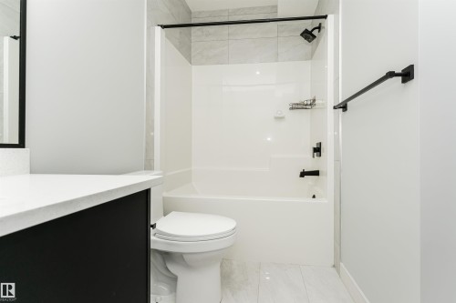 Bathroom featuring a white tub/shower combination with black fixtures, a dark vanity with a light countertop, and a white toilet - 5386 Kimball Place, Edmonton, AB - Indoor Photo Showing Bathroom