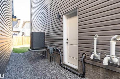 Exterior utility area featuring gravel ground cover, gray horizontal siding, and a white side entry door - 5386 Kimball Place, Edmonton, AB - Outdoor With Exterior