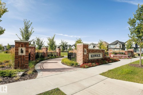 Brick and stone community entrance featuring a paved pathway, stone-capped pillars, and established landscaping - 5386 Kimball Place, Edmonton, AB - Outdoor