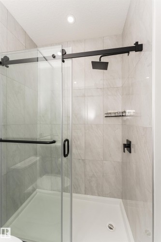 Shower enclosure featuring a sliding glass door with matte black hardware, textured tile walls, a built-in shower bench, a rain showerhead, and a recessed ceiling light - 5386 Kimball Place, Edmonton, AB - Indoor Photo Showing Bathroom