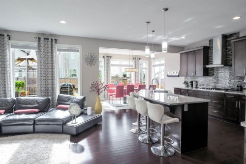 Open-concept living space featuring wood-finish flooring throughout, a kitchen island with seating, dark wood cabinetry, and a full tile backsplash - 1728 53 Street, Edmonton, AB - Indoor