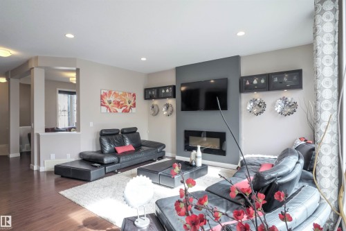 Living area featuring dark wood-finish flooring, recessed lighting, and a modern fireplace with a wall-mounted media panel - 1728 53 Street, Edmonton, AB - Indoor Photo Showing Living Room With Fireplace