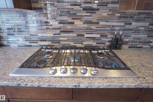 Stainless steel gas cooktop with five burners set into a speckled stone countertop - 1728 53 Street, Edmonton, AB - Indoor