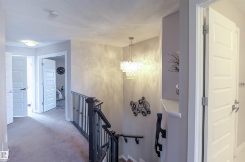 Upper-level hallway featuring a contemporary tiered chandelier, dark wood railing with metal balusters, and a light gray carpeted floor - 1728 53 Street, Edmonton, AB - Indoor Photo Showing Other Room